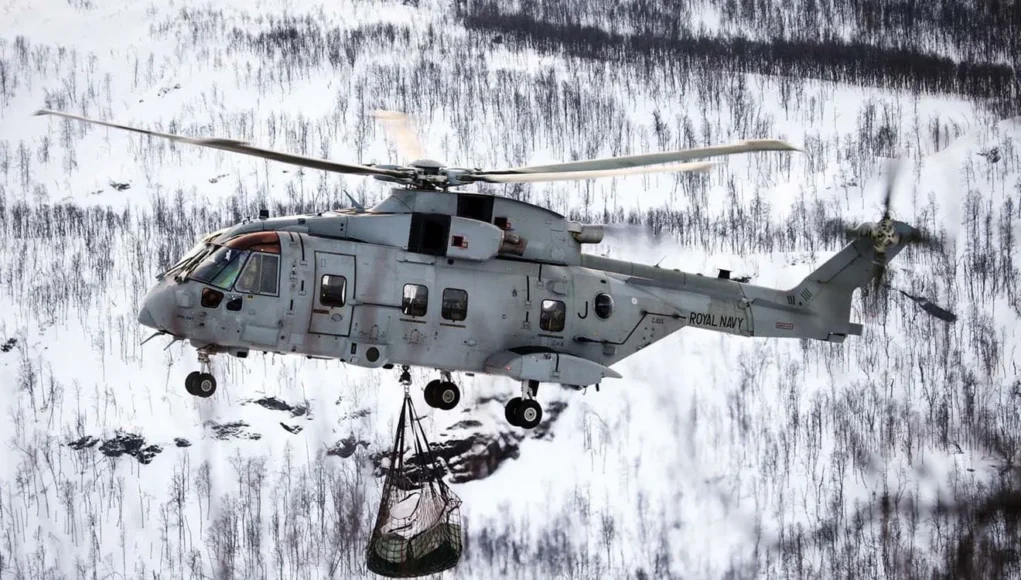 A Merlin Mk4 carries the load of logs over the snow-covered landscape