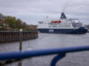 DFDS cruise ship moored in a harbor, viewed from a walkway with a blue railing in the foreground.