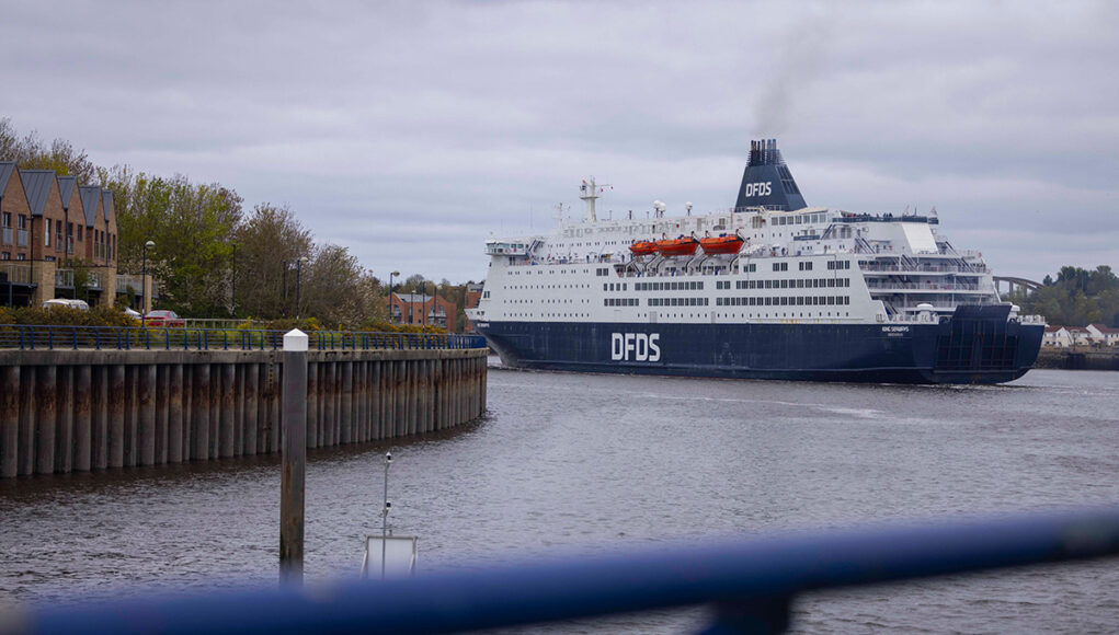DFDS cruise ship moored in a harbor, viewed from a walkway with a blue railing in the foreground.