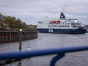 DFDS cruise ship moored in a harbor, viewed from a walkway with a blue railing in the foreground.