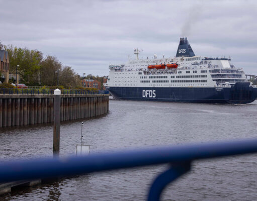 DFDS cruise ship moored in a harbor, viewed from a walkway with a blue railing in the foreground.
