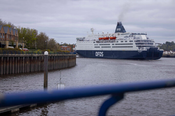 DFDS cruise ship moored in a harbor, viewed from a walkway with a blue railing in the foreground.