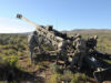 Soldiers in camouflage work around a large field artillery gun in a desert training area.