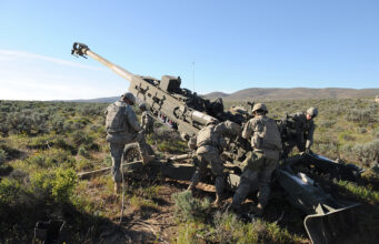 BAE unveils new digital artillery fire control system Soldiers in camouflage work around a large field artillery gun in a desert training area.