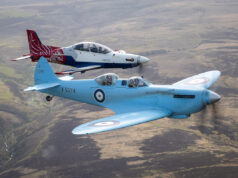 Two vintage RAF training aircraft fly in formation over rolling countryside, one blue with roundels in the foreground and a red‑white aircraft behind it.
