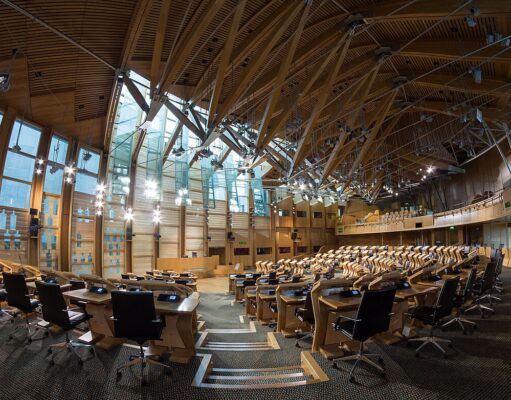 Large modern parliamentary chamber with curved wood benches and black office chairs in rows.