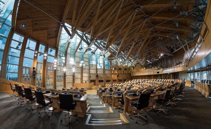 Large modern parliamentary chamber with curved wood benches and black office chairs in rows.