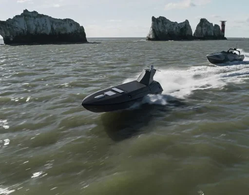 Two black speedboats race across choppy green water near rugged rocky islets with a distant red-and-white lighthouse on the horizon.