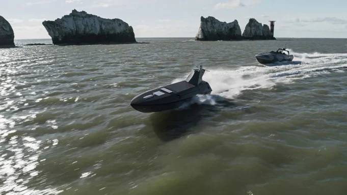 Two black speedboats race across choppy green water near rugged rocky islets with a distant red-and-white lighthouse on the horizon.