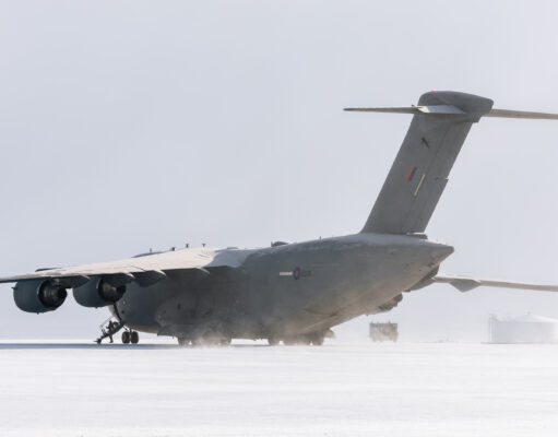 Large military transport aircraft (four engines) on a snow-covered tarmac with a ground crew member nearby.