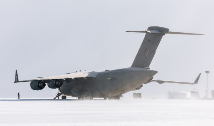 Large military transport aircraft (four engines) on a snow-covered tarmac with a ground crew member nearby.