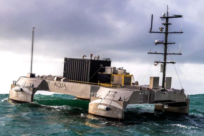 Metallic, rectangular research catamaran riding rough seas with a tall mast and lab equipment on deck.