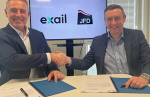 Two men in blazers shake hands over a table while signing documents, with Exail and JFD logos on screen behind them.