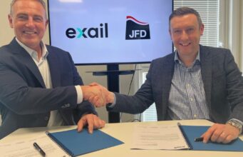 Two men in blazers shake hands over a table while signing documents, with Exail and JFD logos on screen behind them.