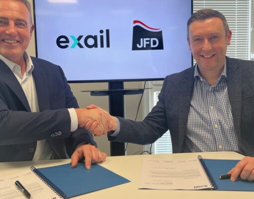 Two men in blazers shake hands over a table while signing documents, with Exail and JFD logos on screen behind them.