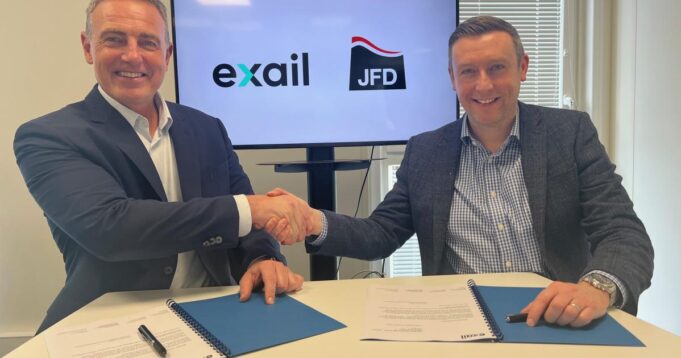 Two men in blazers shake hands over a table while signing documents, with Exail and JFD logos on screen behind them.