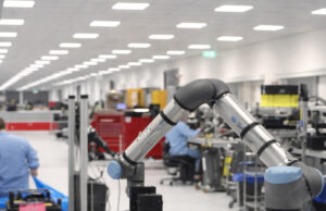 Industrial robotic arm on a production line with workers at benches in a bright factory.