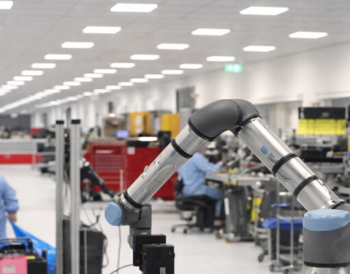 Industrial robotic arm on a production line with workers at benches in a bright factory.