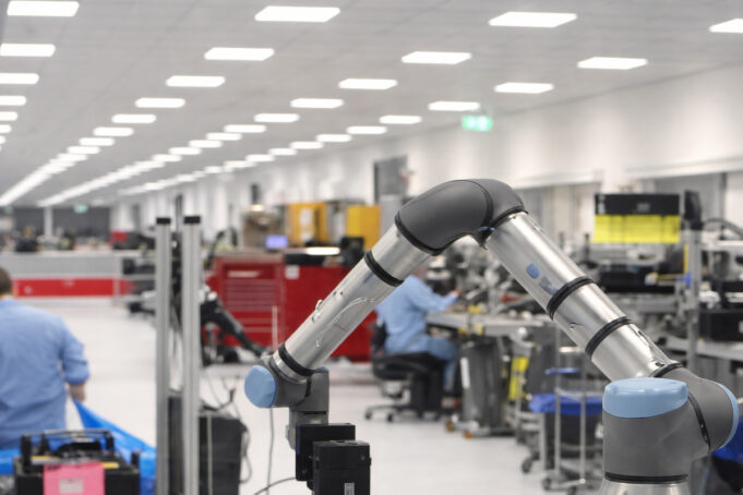 Industrial robotic arm on a production line with workers at benches in a bright factory.