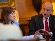Healey quits as Defence Secretary over funding row Two professionals sit at a meeting table, the woman in a light blue blazer listening as the man in a dark suit and red tie speaks gesturing with his hands.