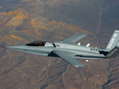 Gray stealth jet flying over arid desert mountains, cockpit visible and tail marked TALON Q with registration on fuselage