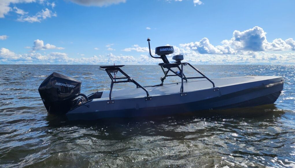 Gray small boat with a Mercury outboard powered engine on open water under a blue sky with clouds.