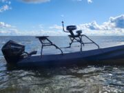 Gray small boat with a Mercury outboard powered engine on open water under a blue sky with clouds.