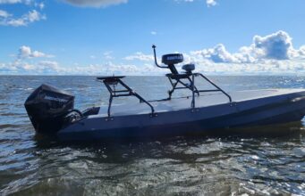 Gray small boat with a Mercury outboard powered engine on open water under a blue sky with clouds.