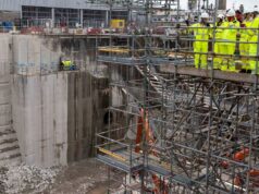 First Sea Lord visits Babcock Devonport site to view work Construction site with workers in high-visibility suits and hard hats on scaffolding above a deep concrete excavation pit.