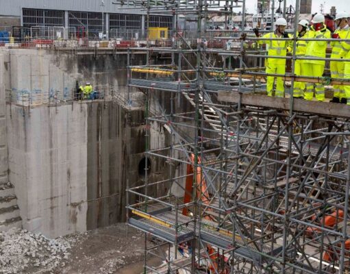 First Sea Lord visits Babcock Devonport site to view work Construction site with workers in high-visibility suits and hard hats on scaffolding above a deep concrete excavation pit.