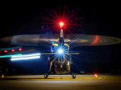 Front view of a helicopter on a night runway, rotor blades blurred by motion and bright front light.