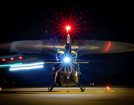 Front view of a helicopter on a night runway, rotor blades blurred by motion and bright front light.