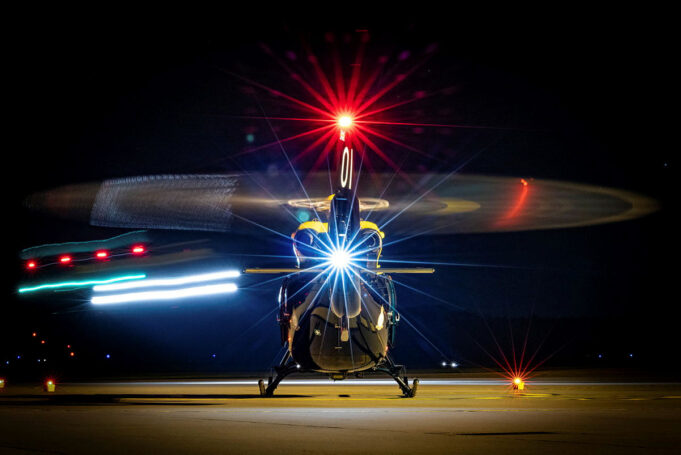 Front view of a helicopter on a night runway, rotor blades blurred by motion and bright front light.