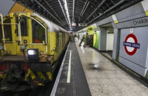 Yellow maintenance locomotive on a London Underground platform at Charing Cross, with green wall tiles and passengers in the background.