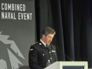 Military officer in dress uniform delivering a speech at a podium during a Combined Naval Event.
