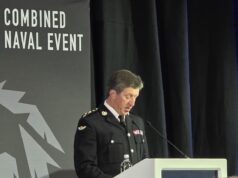 Military officer in dress uniform delivering a speech at a podium during a Combined Naval Event.