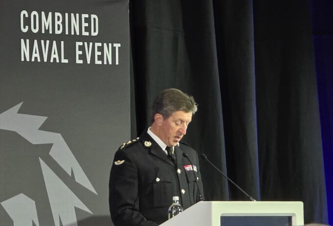 Military officer in dress uniform delivering a speech at a podium during a Combined Naval Event.