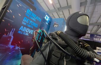 JFD talks military diving demands and new rebreather at CNE Life-size deep-sea diver suit with hoses on display at a trade show, blue signage reading 'Beneath the waves beyond the limits above all else' in the background.