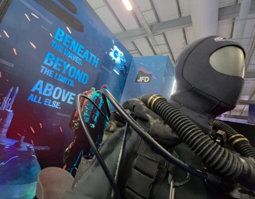 JFD talks military diving demands and new rebreather at CNE Life-size deep-sea diver suit with hoses on display at a trade show, blue signage reading 'Beneath the waves beyond the limits above all else' in the background.