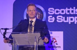 UK sets out how the 50m Scotland defence deal will be spent Man in a dark suit giving a speech at a clear podium with microphones, blue stage backdrop reading 'Scottish & Supply' and event signage nearby