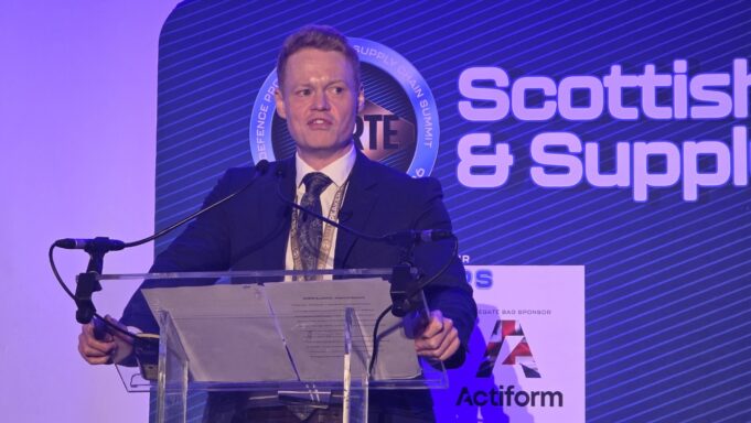 UK sets out how the 50m Scotland defence deal will be spent Man in a dark suit giving a speech at a clear podium with microphones, blue stage backdrop reading 'Scottish & Supply' and event signage nearby