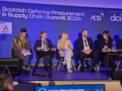 Panel of six speakers seated on a stage at the Scottish Defence Procurement & Supply Chain Summit 2026, with a blue backdrop and sponsor logos behind them.