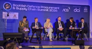 Panel of six speakers seated on a stage at the Scottish Defence Procurement & Supply Chain Summit 2026, with a blue backdrop and sponsor logos behind them.