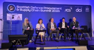 Five panelists seated on stage at the Scottish Defence Procurement & Supply Chain Summit 2026, with a blue-lit backdrop and sponsor logos.