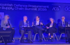 DPRTE Scotland shows SMEs how to win defence contracts Five panelists seated on stage during the Scottish Defence Procurement & Supply Chain Summit 2026, blue-lit backdrop with sponsor logos.