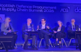 Five panelists seated on stage during the Scottish Defence Procurement & Supply Chain Summit 2026, blue-lit backdrop with sponsor logos.