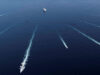 All ten JEF nations sign up to British northern navies plan Aerial view of several ships at sea leaving white wake trails that intersect on the deep blue ocean.