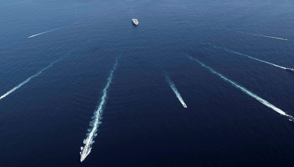 20260521_141913 Aerial view of several ships at sea leaving white wake trails that intersect on the deep blue ocean.