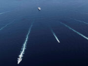 Aerial view of several ships at sea leaving white wake trails that intersect on the deep blue ocean.