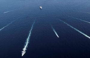 Aerial view of several ships at sea leaving white wake trails that intersect on the deep blue ocean.